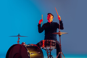 Caucasian male drummer improvising isolated on blue studio background in neon light. Performing,...