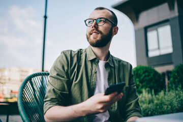 Thoughtful hipster guy updating profile on telephone device using high speed internet connection