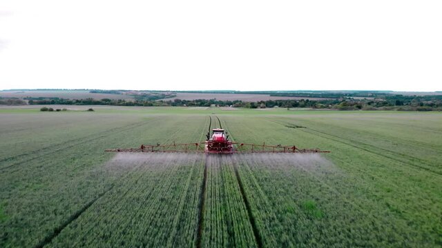 Farmer irrigates the green field. Chemical treatment of the field with pesticides and protection against insects of rodents, parasites and pests. Aerial view of tractor spraying crop in field