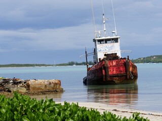 Naklejka premium A rusty fishing boat is docked by the shores of a white sand beach in George Town, Bahamas