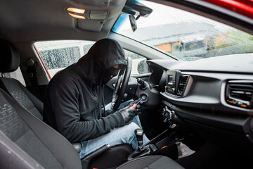 Side view of theft in balaclava and leather gloves using screwdriver in car