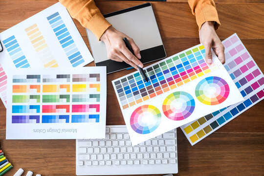 Image of female creative graphic designer working on color selection and drawing on graphics tablet at workplace with work tools and accessories, top view workspace