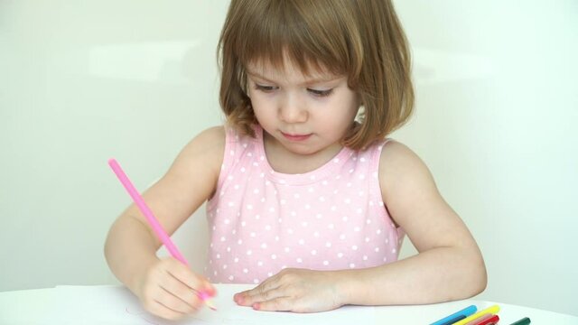 Portrait of little smiling 3 year old child girl draws with pencils on paper sitting at white table at home. Education concept. Children's creativity. Close up