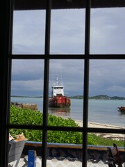 Window view of the beach with a shipwrecked fishing boat docked by the shores in a tropical island
