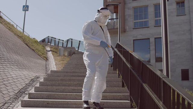 Man in protective suit disinfects street with an antiseptic sprayer. Surface treatment due to coronavirus disease. Virus pandemic and protection concepts.