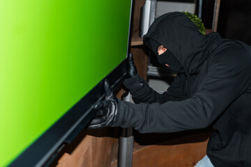 Side view of robber in mask and leather gloves holding tv during stealing