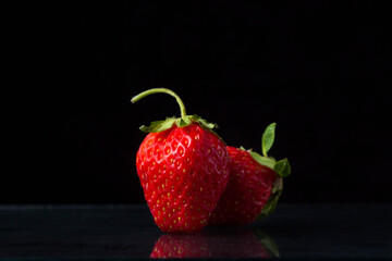 Two strawberries on a black background. One strawberry is standing, the other is lying nearby. Creative photo of strawberries