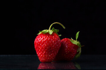 Two strawberries on a black background. One strawberry is standing, the other is lying nearby. Creative photo of strawberries