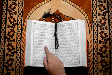 Muslim woman reading the Holy Quran using the finger. The Holy Quran on the mat of prayers . Top...