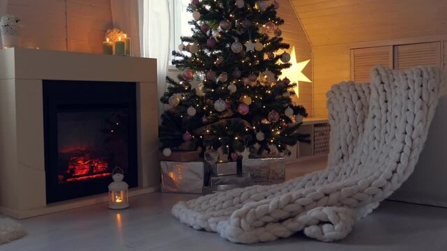 Christmas celebration in cozy interior with decorated spruce tree, fireplace and merino plaid. Winter holidays