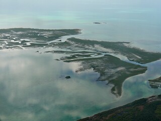 The islands of the Exuma Cays surrounded by clear blue waters of the Bahamas seen from an airplane window
