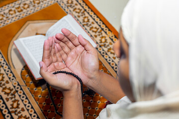 Muslim Asian women raise their hands to pray on the mat at home. Indoors. Focus on hands.