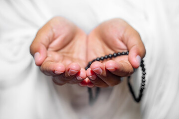 Muslim women raise their hands to pray with a Tasbeeh on white background, indoors. Focus on hands.