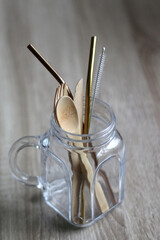 Wooden cutlery and reusable metal straws in a glass jar. Selective focus.