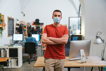 Portrait of leader of a startup in the office with medical mask for protection and prevention...