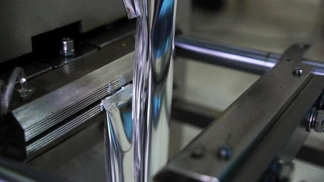 Food sachets of silver color are made on the technical device created for packing of foodstuff. Close-up.