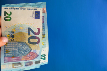 A woman's hand holds several twenty-Euro bills on a bright blue background. The concept of cash, give money on credit, pay in cash