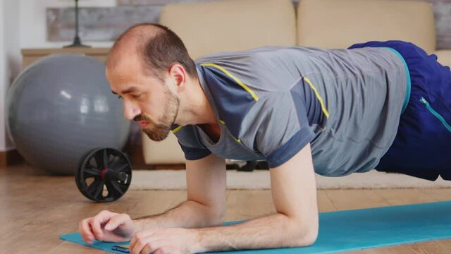 Fit man doing plank exercise at home on yoga mat wearing sportswear. Sport at home and healthy lifestyle, activity, fitness and workout. Indoor training and home exercise