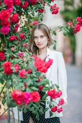 Young beautiful woman walks in a European city. Portrait of a young woman near blooming roses. Europe.