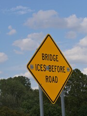 Road sign “Bridge ices before road” in a grassy patch near a bridge