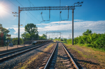 Fototapeta na wymiar Railway station at bright sunny day in summer. Railroad in Europe. Heavy industry. Industrial landscape with railway platform, green trees, blue sky with clouds and sunlight. Transportation