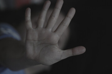 Fototapeta premium The palm of a female hand giving the signal to stop. The dark, moody image is a concept of a woman being abused, raped, beaten, threatened, robbed, domestic violence etc. A sign of the #metoo movement