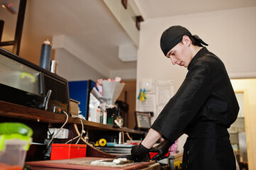 Professional chef wear in black making sushi and rolls in a restaurant kitchen of japanese traditional food.