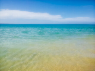 Turquoise ocean background with small island or hill on part of horizon and beach visible under water up close - room for copy