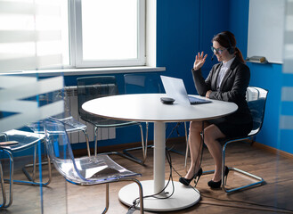 Friendly woman wearing a headset is having an online conversation on a laptop in a conference room. Female manager communicates with clients via video call. Remote business negotiations in quarantine.