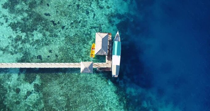 Sunny aerial view of a boat moored to a pontoon in the beautiful blue lagoon of Kanawa island, near the city of Labuan Bajo on Flores, Indonesia