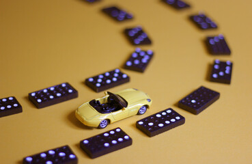A toy car and domino pieces on yellow background 