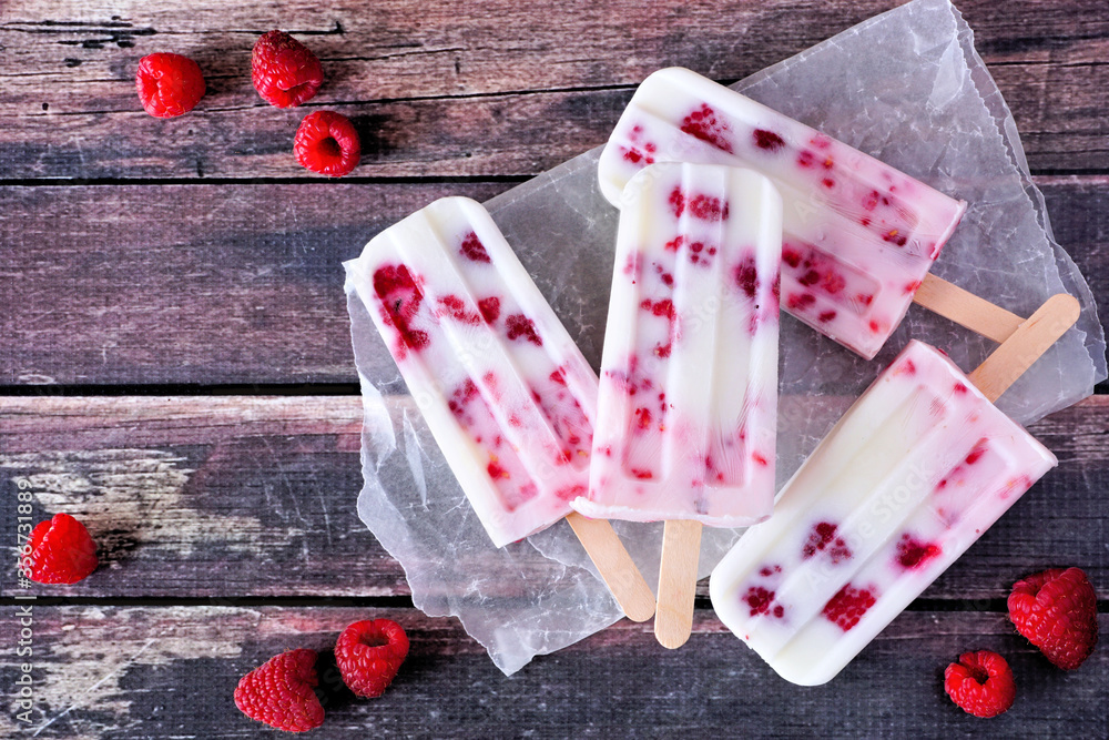 Poster homemade raspberry vanilla yogurt ice pops. overhead table scene on a rustic dark wood background.