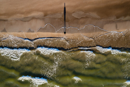 Aerial view of person silhouette shadow standing on Baltic sea shore beach in Klaipeda, Lithuania. Perspective of beautiful nature patterns on surface.
