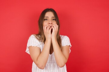 Anxiety - a conceptual image of a beautiful young caucasian woman covering her mouth with her hands and standing outdoors. Scared from something or someone bitting nails.