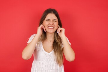 Stop making this annoying sound! Headshot of unhappy stressed out young female making worry face, plugging ears with fingers, irritated with loud noise coming from neighbours who live above her.