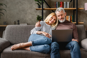 Senior couple using laptop and smiling while resting on couch at homewhile watching movie