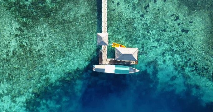 Static aerial view of a boat moored to a pontoon in a beautiful blue lagoon surrounded by coral reef. Kanawa island, near the city of Labuan Bajo on Flores, Indonesia
