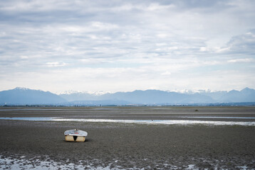 Obraz premium Boat siting on the ground during outflow with cloudy sky and mountains in backdrop, shot in Vancouver, British Columbia, Canada