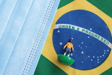 flag of Brazil with plastic football player and surgical mask for Coronavirus Prevention - Covid19 pandemic
