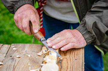 a man carves a wooden spoon with a metal tool