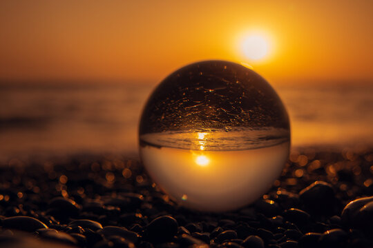 Stones on the ocean shore and waves and splash is reflected in a crystal ball at sunset