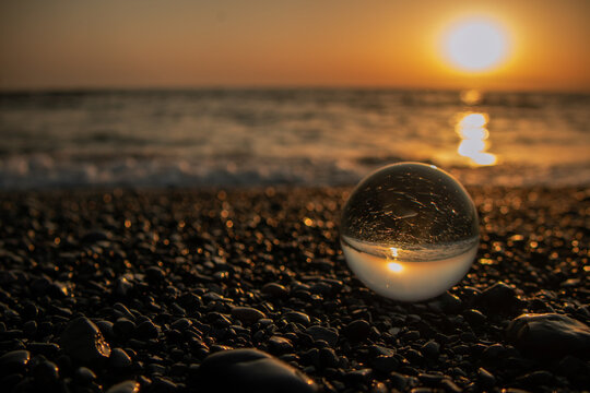 Stones on the ocean shore and waves and splash is reflected in a crystal ball at sunset