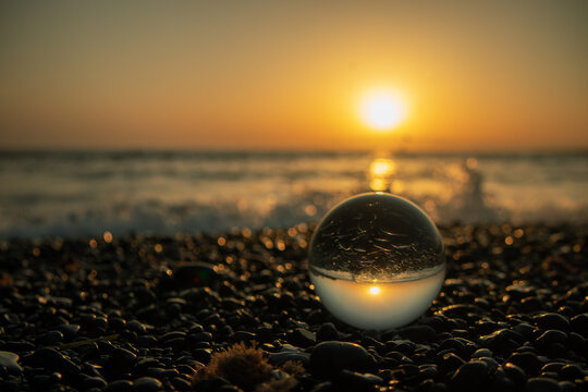 Stones on the ocean shore and waves and splash is reflected in a crystal ball at sunset
