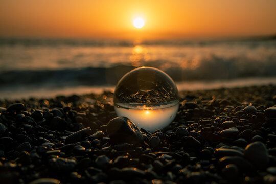 Stones on the ocean shore and waves and splash is reflected in a crystal ball at sunset