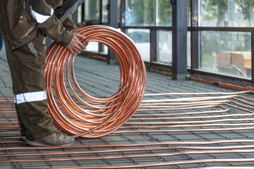 Plumber laying copper pipes on floor with warm heating