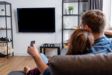selective focus of man holding remote controller and looking at flat panel tv with blank screen...