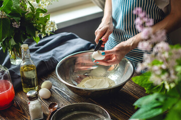 A woman is breaking an egg to make dough. Making handmade pasta in a pleasant and cozy home environment