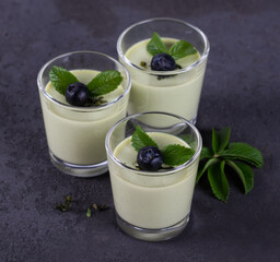 Dessert cream Panna cotta with green tea matcha and blueberries in a glass on a dark background