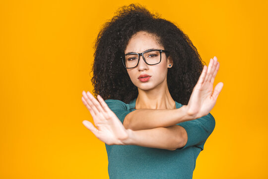 Close Up Portrait Of A Serious Young African American Woman Showing Stop Or No Gesture With Her Palm Isolated Over Yellow Background.