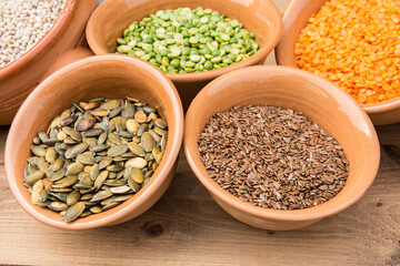 Small clay bowls with various seeds: pumpkin seeds, flaxseed, red lentils, green peas, barley grains.